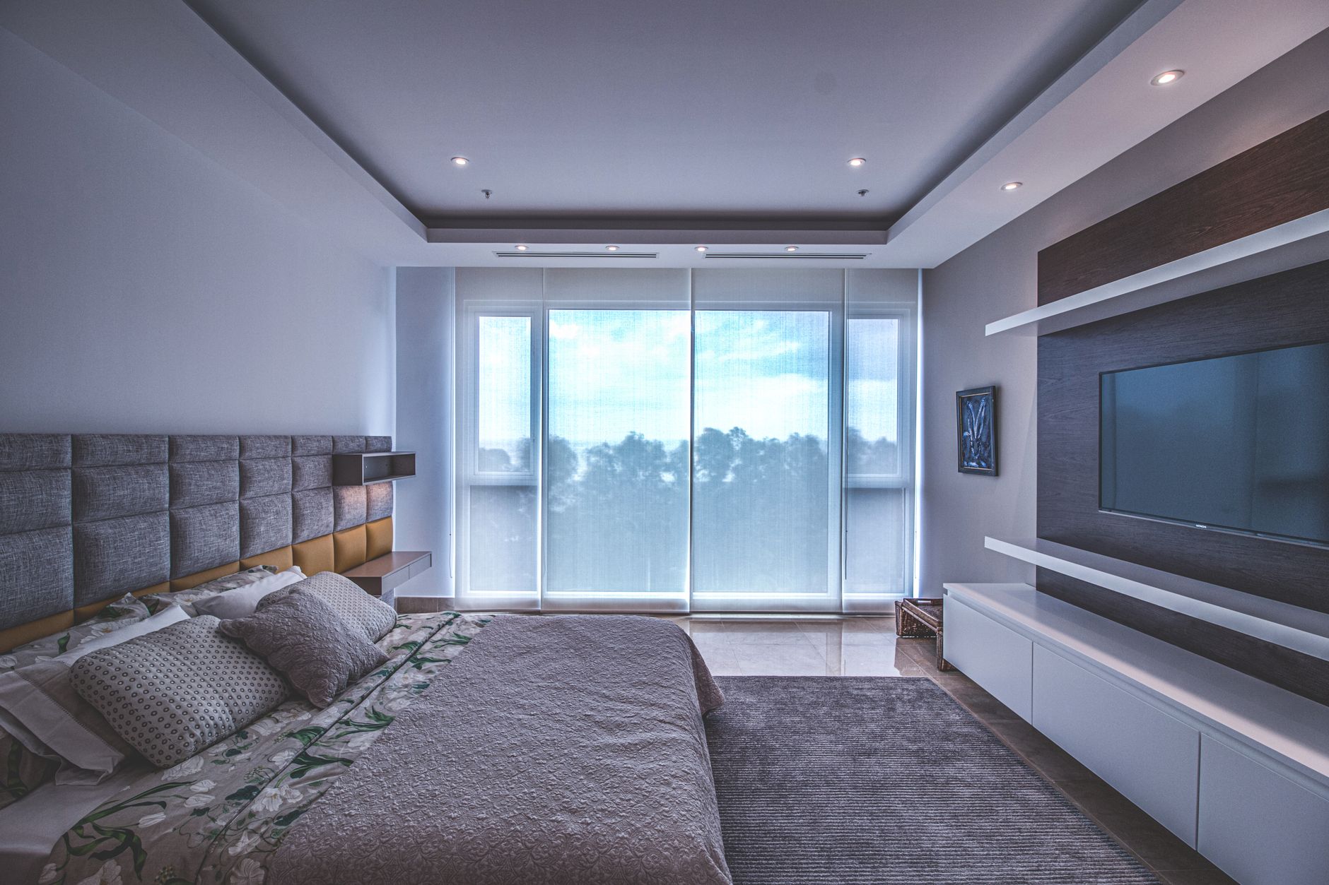 Spacious luxury bedroom with a modern design, featuring a large window and a wall-mounted TV