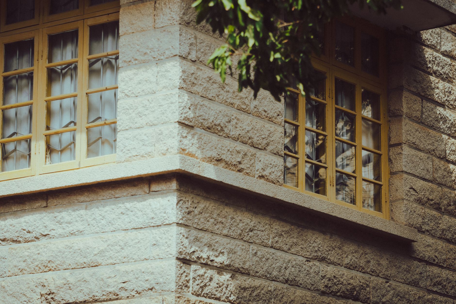 Corner of a stone building with vintage style yellow-framed windows and tree shadows